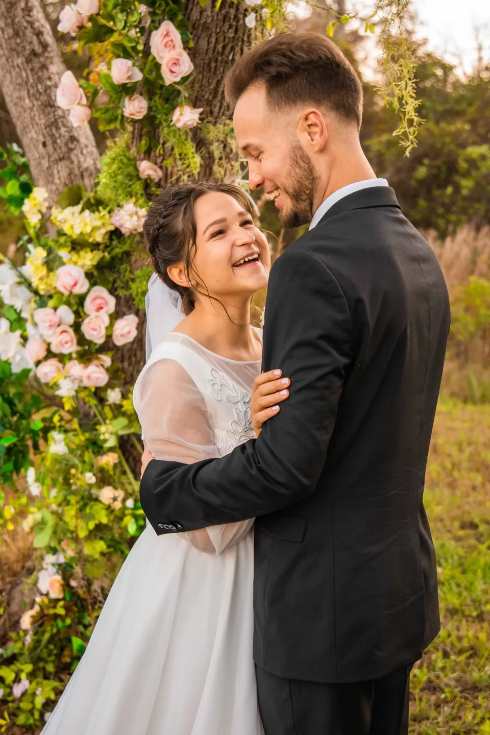 Bride and groom laughing under garden roses at golden hour